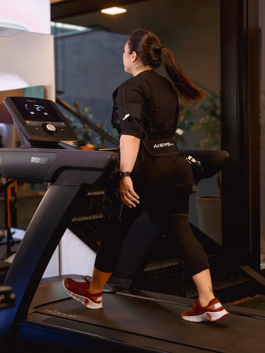 Aluno treinando de eletroestimulação em esteira com painel de acompanhamento na Tecfit